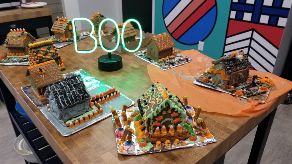 Halloween gingerbread houses made by the Full Stacks team, an illuminated BOO sign at the centre of the table